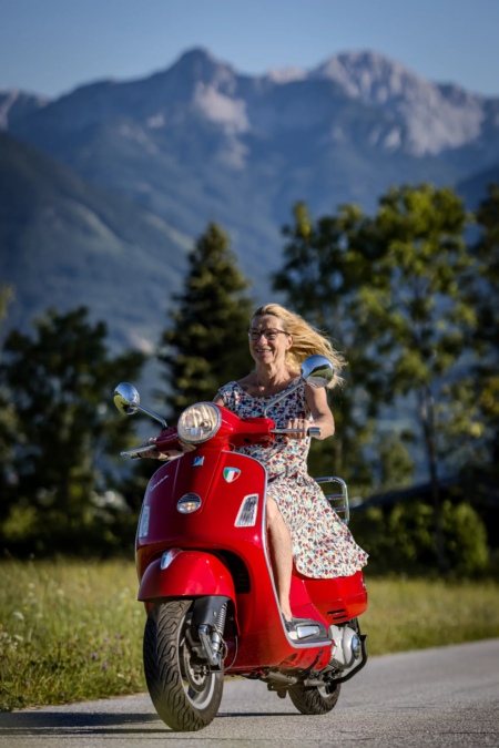 Outdoor-Portrait-gluekliche-Frau-faehrt-auf-roter-Vespa-in-den-Bergen-in-Kaernten Outdoor-Portrait-gluekliche-Frau-faehrt-auf-roter-Vespa-in-den-Bergen-in-Kaernten